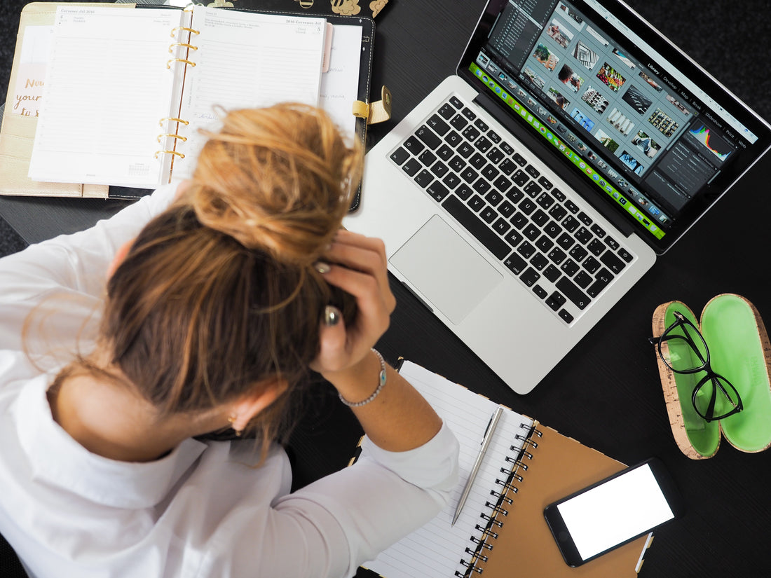 Schreibtisch mit Laptop und Frau die ihren Kopf hält